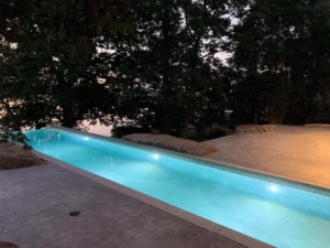 Narrow inground lap pool illuminated at dusk with surrounding trees and stone accents