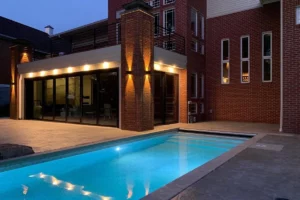 Modern residential lap pool illuminated at dusk beside a brick home