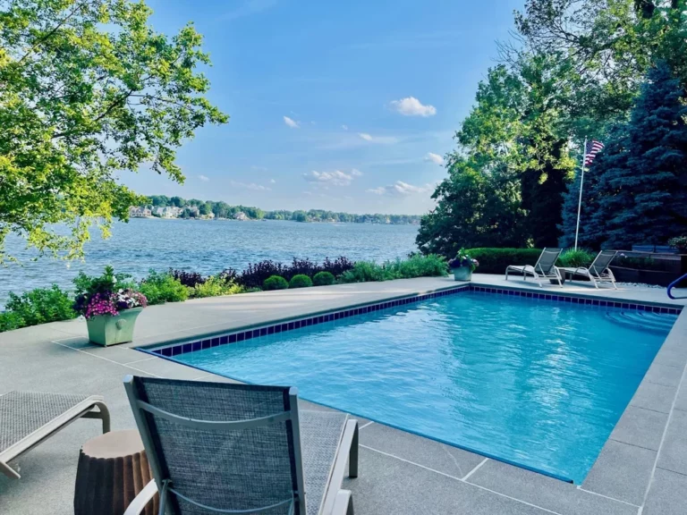 Gunite pool overlooking a lake with surrounding patio seating and landscaping