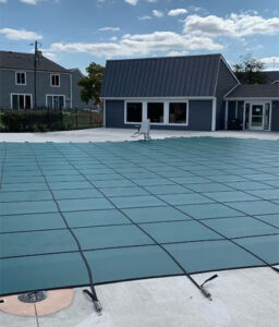 Inground pool secured with a green mesh safety cover on a residential patio