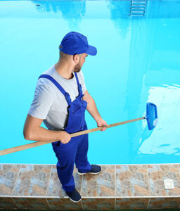 Pool technician skimming debris from a residential swimming pool during routine service