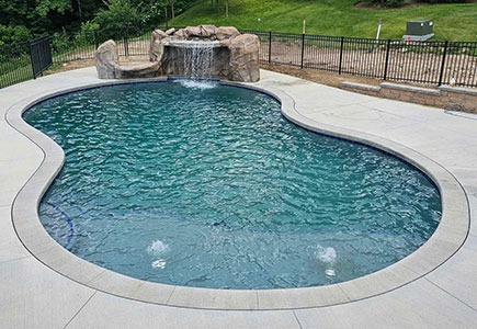 Freeform inground pool with rock waterfall feature and concrete decking