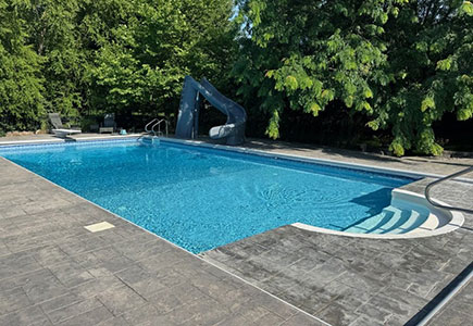 Vinyl inground pool with built-in steps, slide, and textured concrete decking