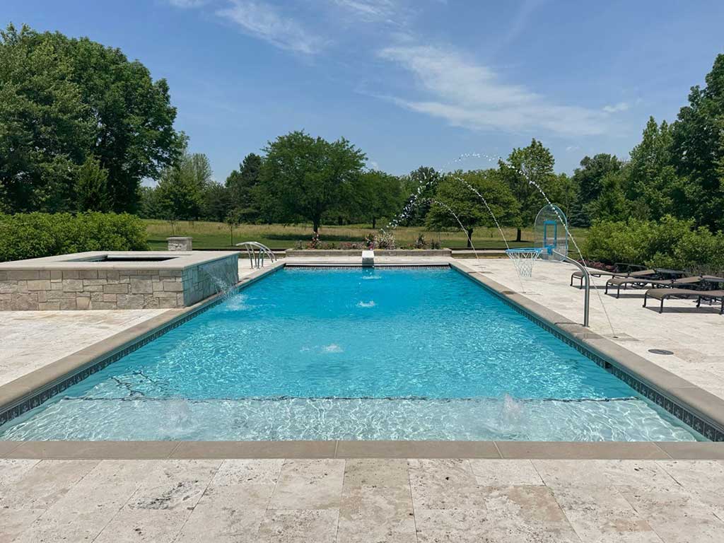 Modern rectangular inground pool with fountain jets, tanning ledge, and stone patio