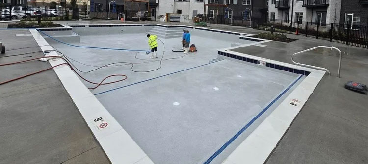 Commercial pool renovation by Barton Pool Company - workers resurfacing large commercial inground pool with light blue finish