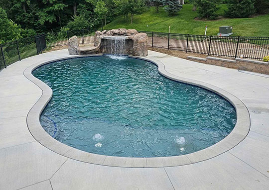 Freeform gunite pool with rock waterfall feature and concrete decking