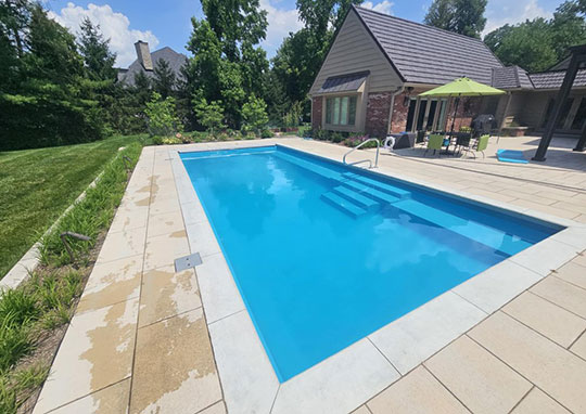 Rectangular fiberglass inground pool with built-in steps and light stone decking