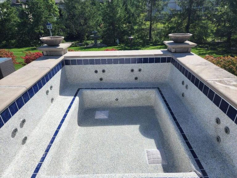 Pool renovation after photo - renovated inground pool with fresh white surface, blue tile border, and gray stone coping by Barton Pool Company