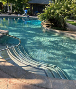 Pool opening service by Barton Pool Company - technician preparing freeform inground pool with crystal clear turquoise water for summer season