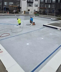 Pool renovation service by Barton Pool Company - workers resurfacing commercial inground pool with light blue finish and tile accents