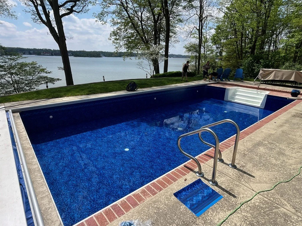 Vinyl liner pool benefits - rectangular inground pool with deep blue patterned liner, brick coping, and lakefront view by Barton Pool Company