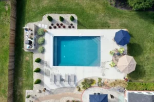 Aerial view of a rectangular vinyl liner pool with surrounding patio, umbrellas, and landscaping