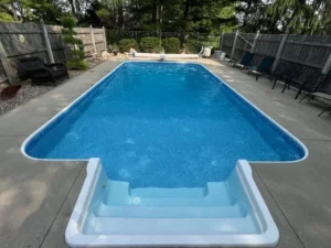 Narrow rectangular vinyl liner pool with molded entry steps and concrete patio