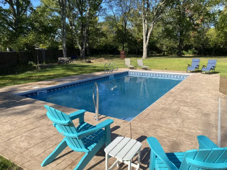 Rectangular vinyl liner pool with stamped concrete deck and bright Adirondack chairs