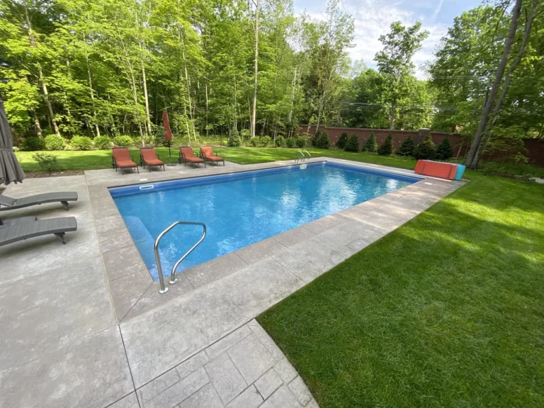 Rectangular vinyl liner pool with concrete deck and lounge chairs in a wooded backyard