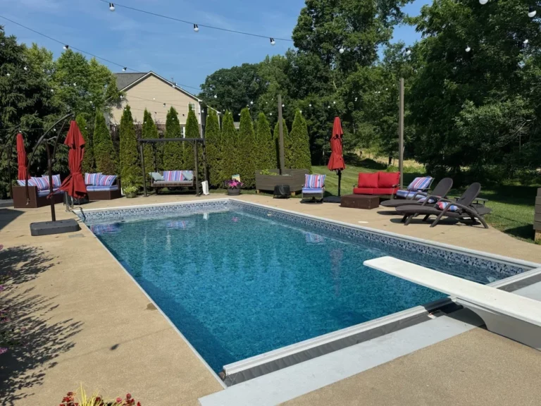 Rectangular vinyl liner pool with diving board, patio seating, and privacy trees