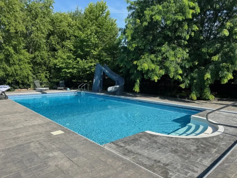 Vinyl liner pool with curved entry steps, stamped concrete deck, and backyard slide