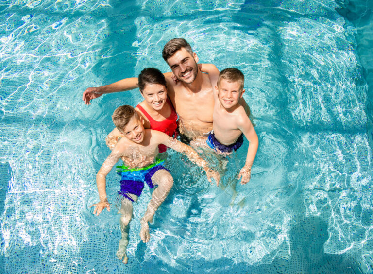 Father and children smiling and swimming together in a clear blue pool